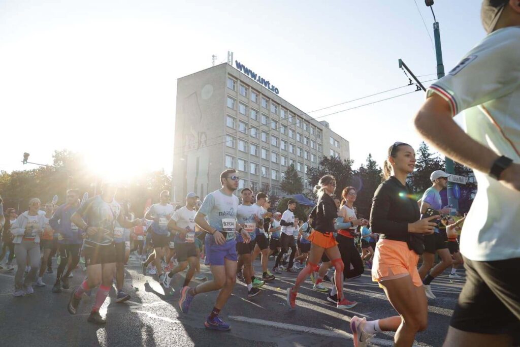 UVT Liberty Marathon – alergători cu numere de concurs pe o stradă din Timișoara, clădirea UVT în fundal