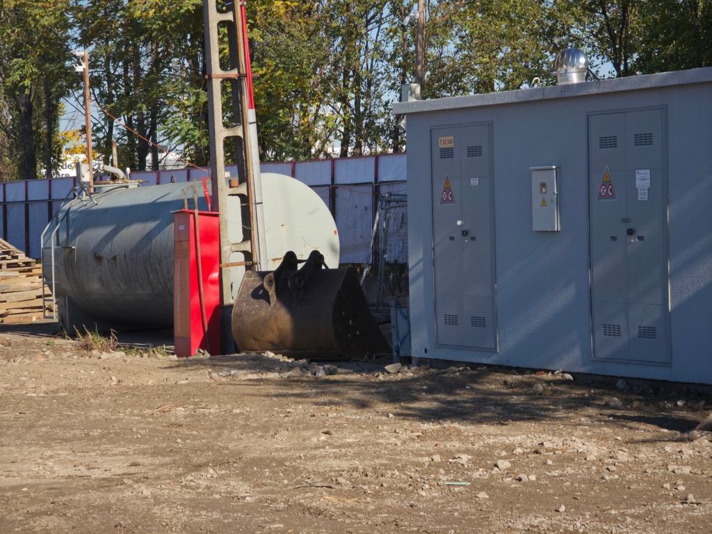 șantier cu cabină electrică, rezervor metalic și cupă de excavator pe teren viran
