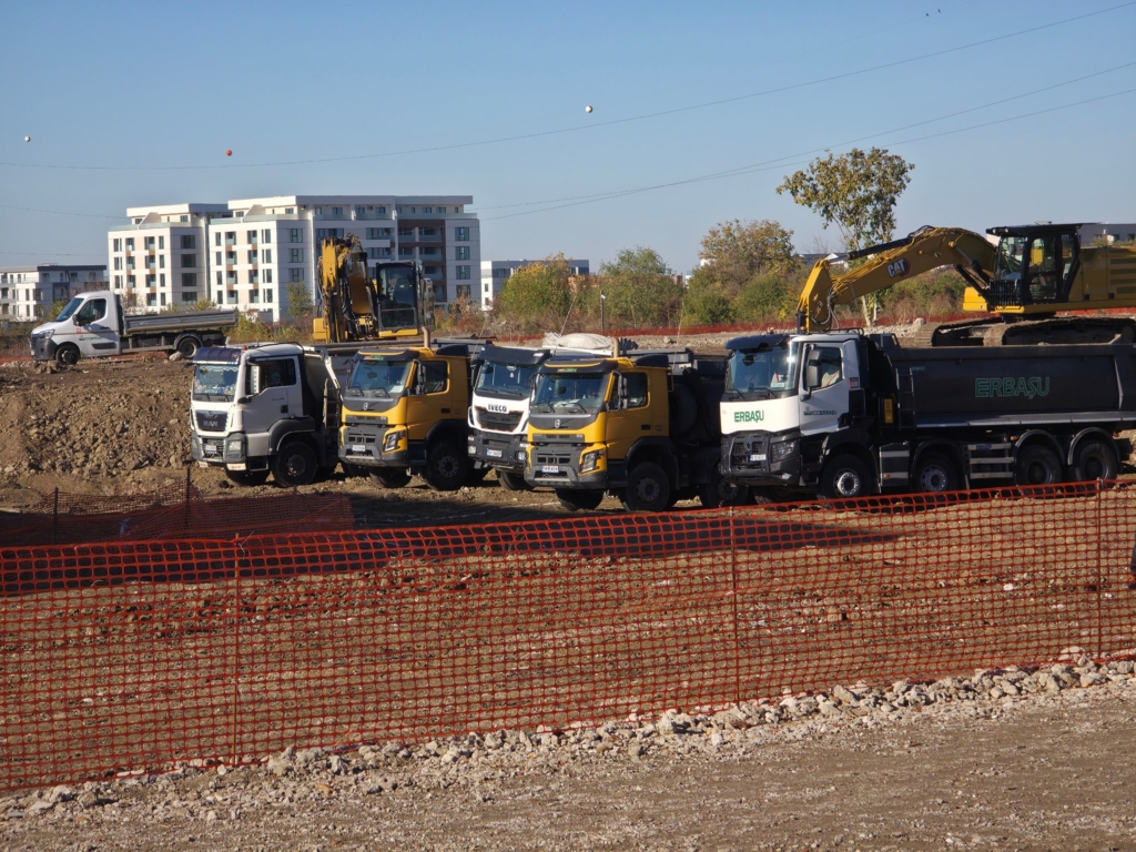 șantier cu camioane basculante și excavatoare, inscripția Erbașu pe un utilaj
