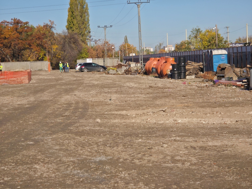 Teren viran cu muncitori, mașină și materiale de construcție pe șantier